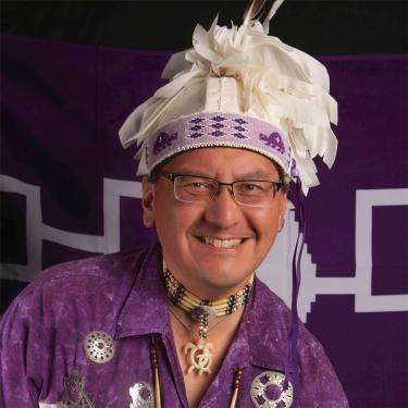 A smiling man wearing a purple top and a headress.