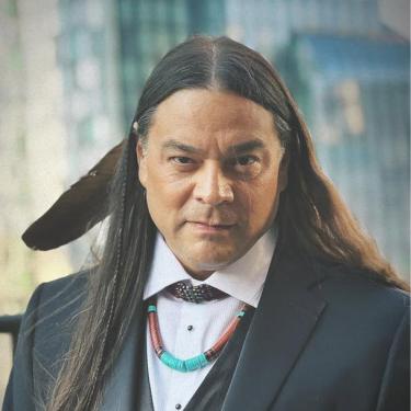 A man wearing a suit with a feather in his hair and a beaded necklace.