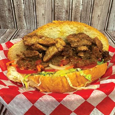 Sandwich with chunks of meat, tomato, onion, lettuce, and sauce on an open bun.