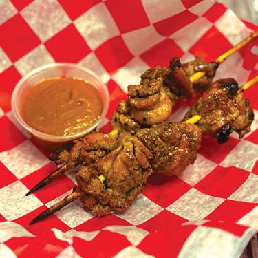 Two skewers with grilled chicken next to a little cup of sauce.