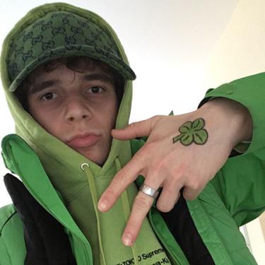 A young person dressed in all green, with a green shamrock painted on their hand.