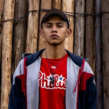 A young man wearing a ball cap, sweatshirt, and red Phillies T-shirt looks directly into the camera.