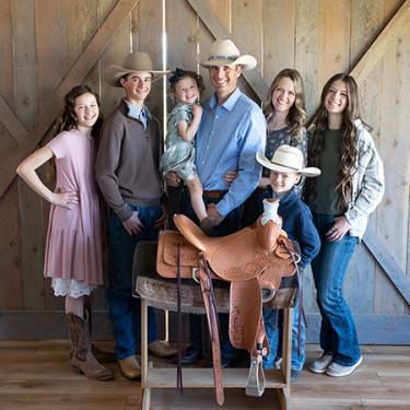 A family of seven pose in front of a horse saddle on a wooden stand.