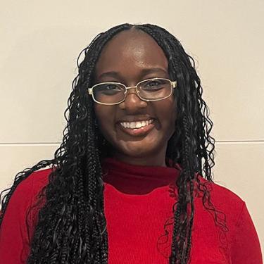 A person with long black braids and a red sweater smiles.