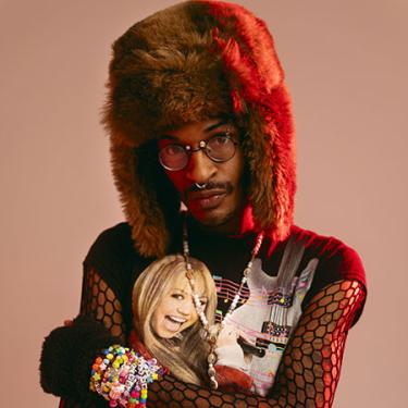 A person poses with a fur cap, fishnet sleeves, and colorful beaded bracelets.
