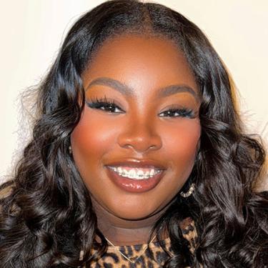 A woman with long wavy dark hair, long blueish eyelashes, and a cheetah-print top smiles.