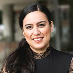 A person with long black hair in a ponytail smiles.