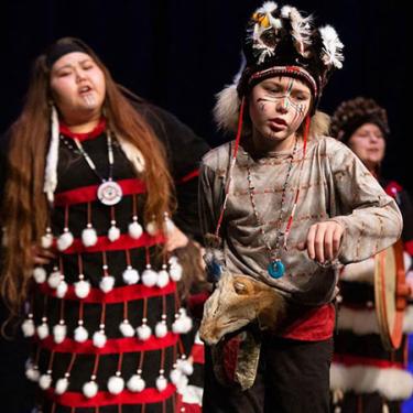 Young people in black regalia with red and white fringe perform on stage.