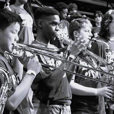Teens play brass instruments. Black-and-white photo.