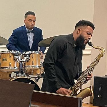 Two men play drums and saxophone.