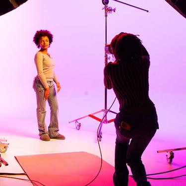 One person poses in a pink-colored studio while another takes photos.