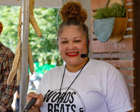 A woman with a high bun, red lipstick, and white Words, Beats & Life Inc. t-shirt smiles at the camera.