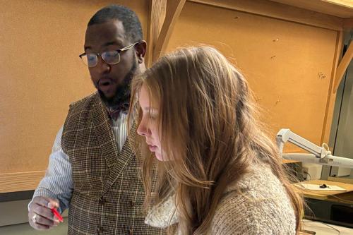 Two young people inspect something out of frame. One holds a pen and looks surprised.