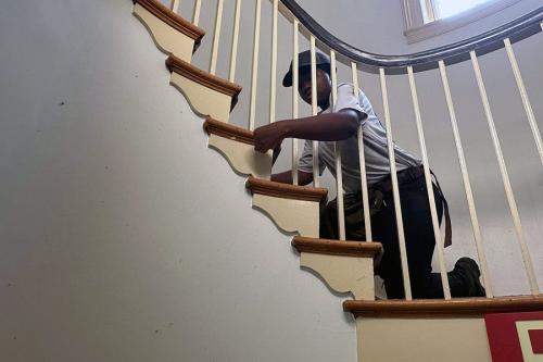 Kneeling on a curving staircase, a person reaches their arm through the vertical posts to adjust a step.