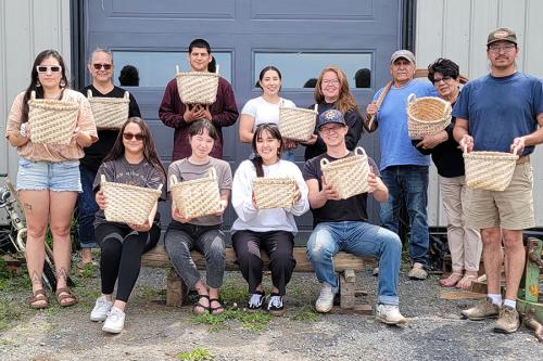 Twelve young and Elder adults pose, each holding up a pale woven basket.