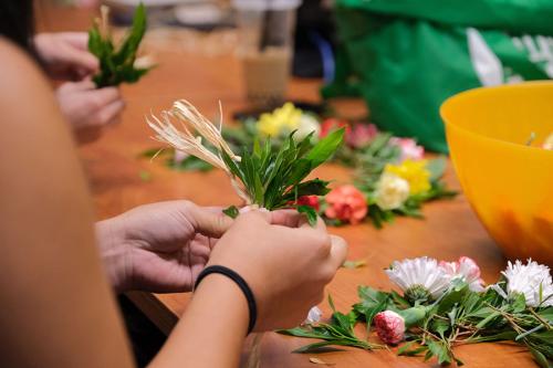 Close-up on hands as they bunch together real or plastic greenery to form Hawaiian leis.