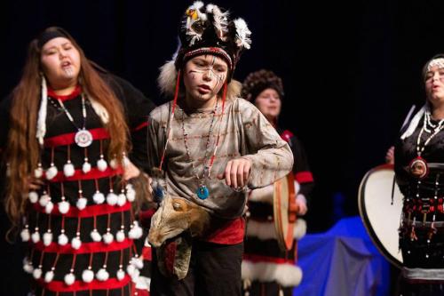 Young people in black regalia with red and white fringe perform on stage.