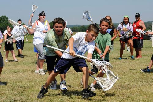 A group of young kids and adults play lacrosse outside.