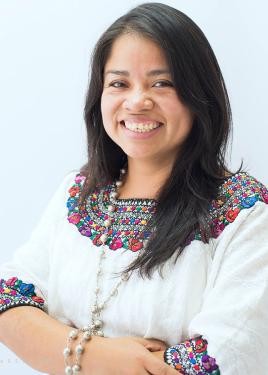 A woman with long dark hair and a white blouse embroidered with rainbow-colored shapes along the neckline.
