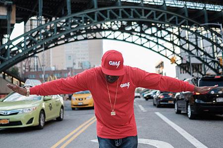 A man in bright red cap and shirt stands in the middle of a busy street, head bowed and arms outstretched.