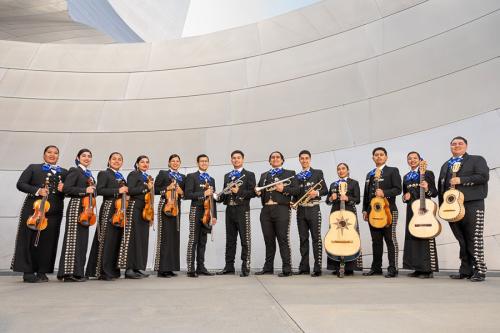 Thirteen young adults pose in black mariachi uniforms holding their instruments: violins, trumpets, and guitars.