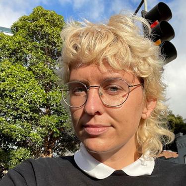 A person with short curly blond hair and glasses smiles at the camera.