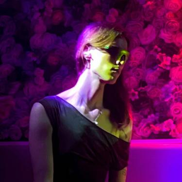 A person with long hair and futuristic sunglasses in front of a floral background.
