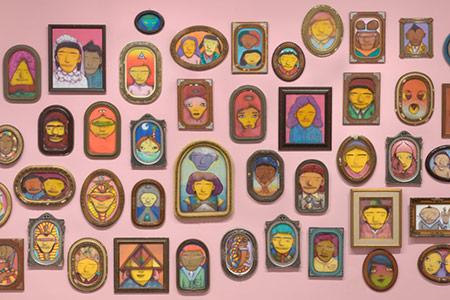 A large group of painted stylized portraits displayed on a pink wall.