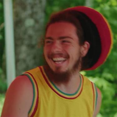 A man with red, yellow, and green hat and tank top laughs.
