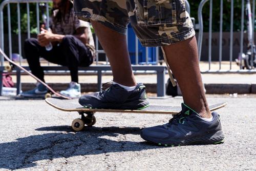 Close-up on the feet of a person in camo cargo shorts and sneakers on a skateboard.