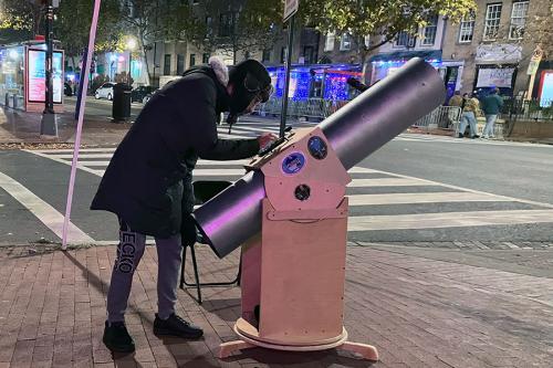 A person operates a large portable telescope on a city street corner at night.