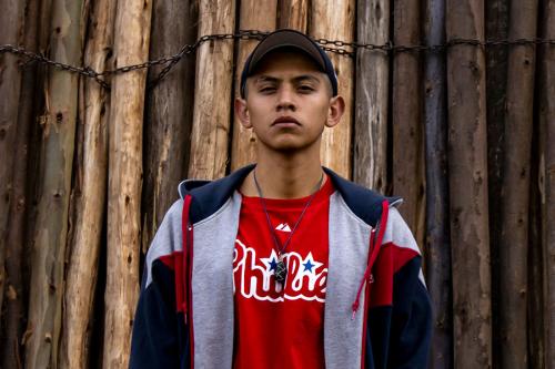 A young man wearing a ball cap, sweatshirt, and red Phillies T-shirt looks directly into the camera.