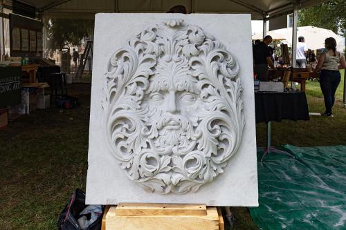 A four- or five-foot tall slab of white stone with the face of a man in swirling foliage chiseled into the surface.