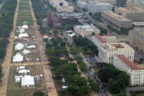Aerial view of the National Mall, showing several white tents in the center of the grass, the Smithsonian Castle, and other government buildings.