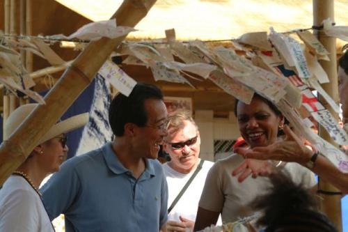 Yo-Yo Ma laughs in conversation with a small group of people among a string of paper strips hung from bamboo poles.