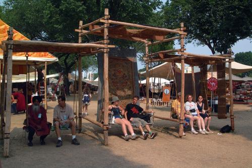 Festival participants and visitors rest in the shade of wooden scaffolding with burlap screens.