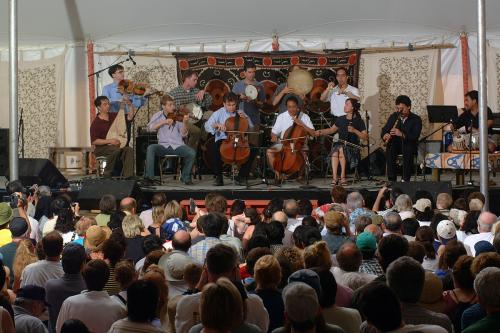 An ensemble with both Western and Eastern classical instrument performs on a stage for a seated audience.