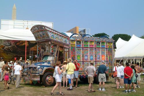 A decorated truck parked on the lawn of the National Mall, with a crowd of people around it and festival tents and the Washington Monument in the background.