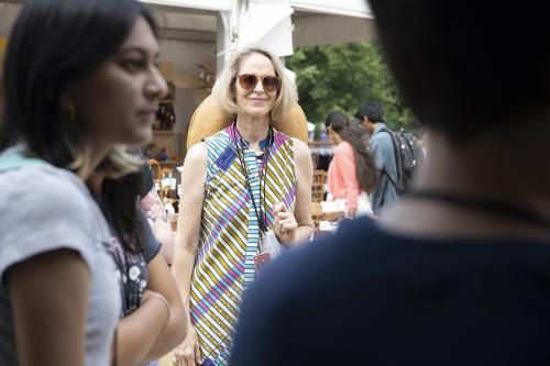 A woman smiles outdoors in a colorful striped dress, framed by people out of focus in the foreground.