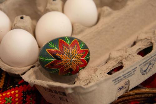 An intricately painted egg with a dark green background and a red flower with orange lines in the middle sits in an egg carton.
