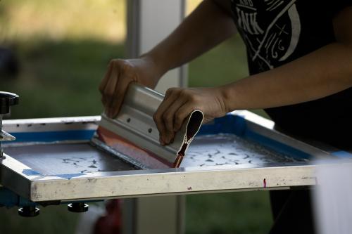 Two hands pull back on a squeegee, scraping paint through a mesh screen.