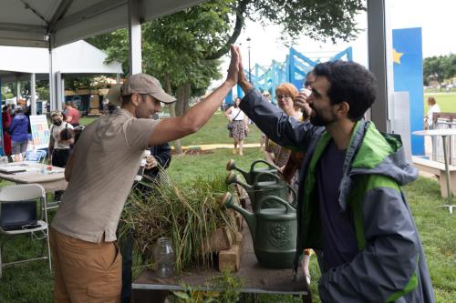 Two people on either side of a table containing potted plants and watering cans high-five.
