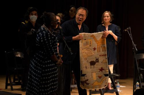 Two people standing on stage. Yo-Yo Ma on the right is holding a small carpet, mouth agape.