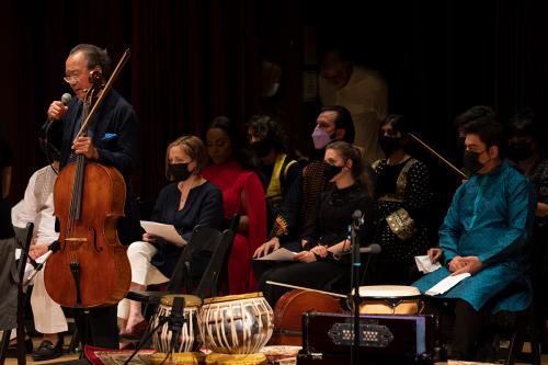 Performers seated on stage, and Yo-Yo Ma, standing with a cello and talking into a microphone, on the left.