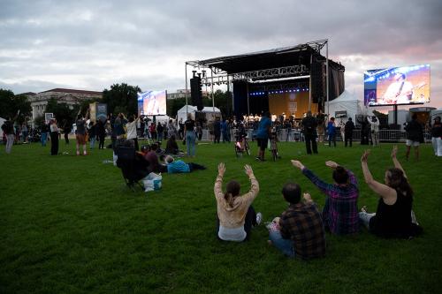 Performers on stage, standing together for a final bow, with audience giving standing ovation in the foreground.