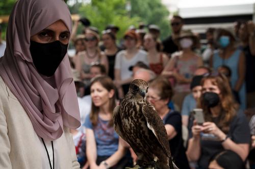 A woman holds a falcon in front of a crowd of people outdoors. 