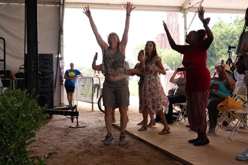 wo women reach their arms out overhead, with more dancing audience members in the background.
