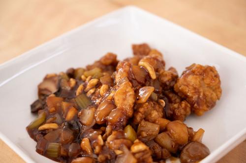 Sauce-covered fried chicken with cashews, onions, and scallions on a white plate.