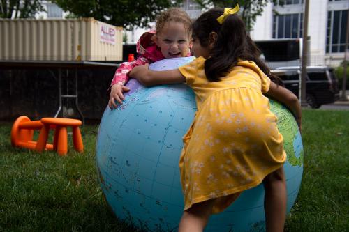 Two young kids embrace a giant inflatable globe, laughing.