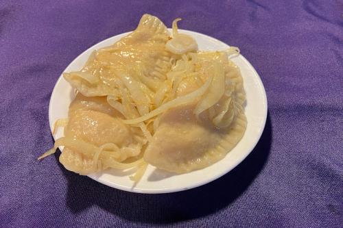 On a plate, three dumplings in the shape of semi-circles with crimped edges, garnished with sauteed onions.